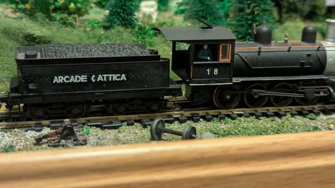 A black model steam locomotive with a coal tender on a miniature train track.